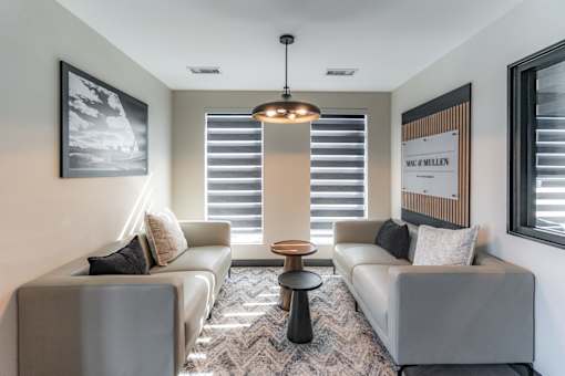 A modern living room with a grey sofa, a round table, and a large window with blinds.
