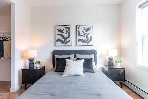 A bedroom with a grey bed and two black nightstands.