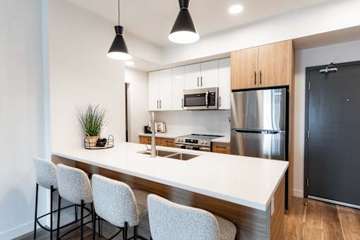 A modern kitchen with a bar area and chairs.at Podium Apartments, Calgary, AB