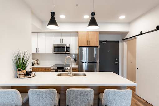 A modern kitchen with a white countertop and grey chairs.at Podium Apartments, Calgary, AB