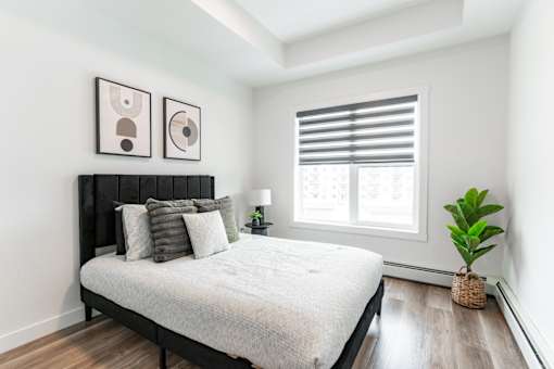 A bedroom with a large bed and two framed pictures on the wall.at Podium Apartments, Calgary, AB