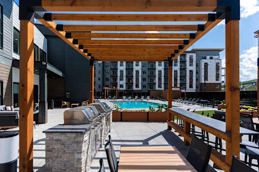 A wooden pergola over a pool area with chairs and a stone pillar.