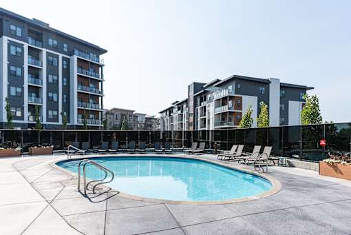 A swimming pool surrounded by lounge chairs and apartment buildings.