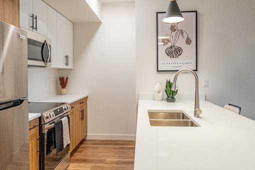 A modern kitchen with a stainless steel refrigerator, wooden cabinets, and a white countertop.at The Artisan at Rangeview, Calgary, Alberta