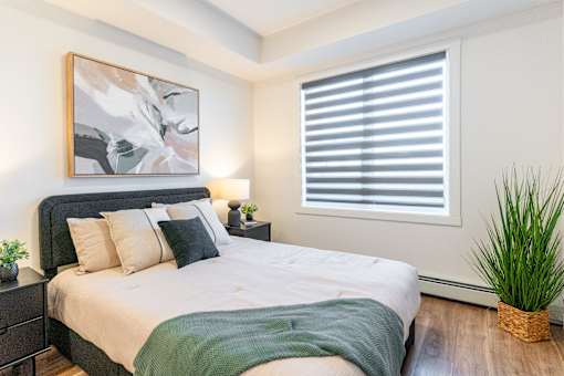 A bedroom with a large bed and a painting on the wall.at The Artisan at Rangeview, Calgary, Alberta