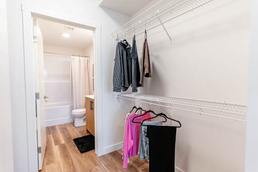 A white bathroom with a toilet, a shower curtain, and a black trash can.at The Artisan at Rangeview, Calgary, Alberta