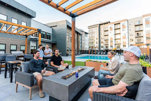 A group of people are sitting around a fire pit on a patio.