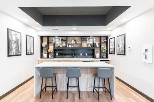 A modern kitchen with a bar area and three grey bar stools.