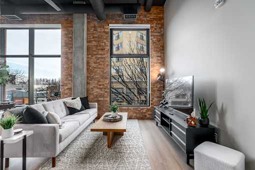 A living room with a grey couch, a wooden coffee table, and a large window with a view of a tree.at Raymond Block, Edmonton Alberta T6E 3R7