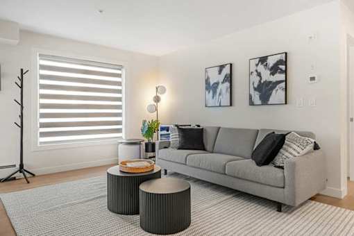 A living room with a grey couch, a round table, and two framed pictures on the wall.