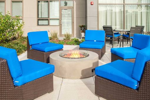 A patio with blue chairs and a fire pit.