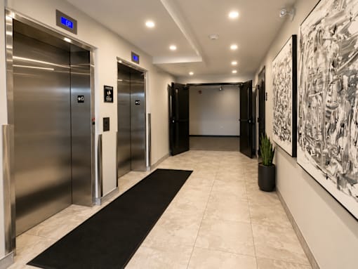 A hallway with two elevators and a large painting on the wall.