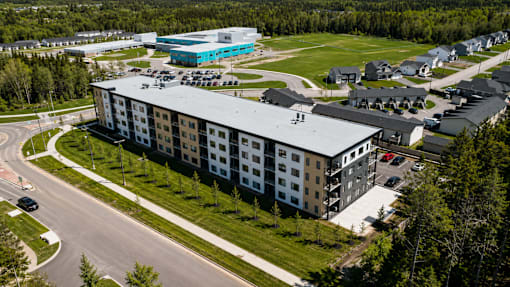 A large building with a blue section on the side is surrounded by trees and other buildings.