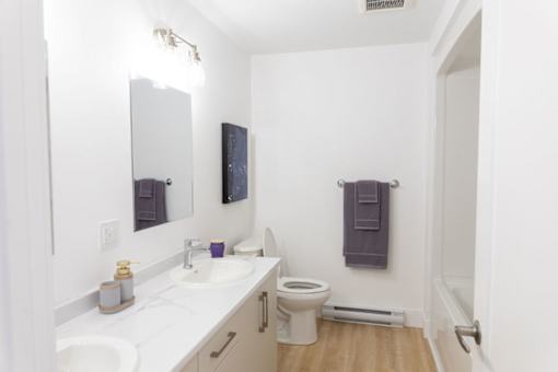 A bathroom with a toilet, sink, mirror and towel rack.