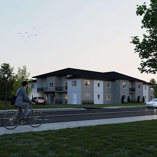 A man in a suit rides a bicycle past apartment buildings.