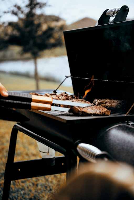A person is grilling steak on a barbecue.
