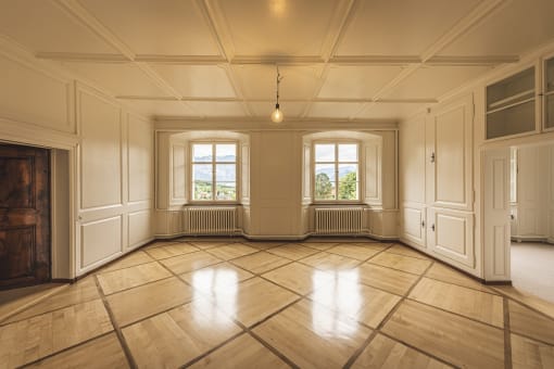an empty living room with wooden floors and two windows