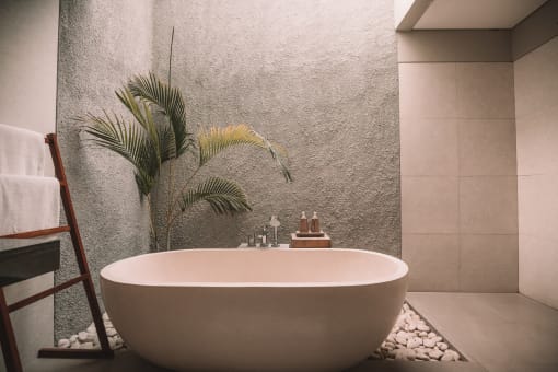 a large white bath tub in a bathroom with a potted plant