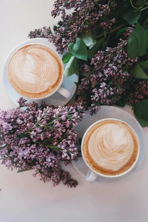 Two cups of coffee with latte art and lilac flowers.