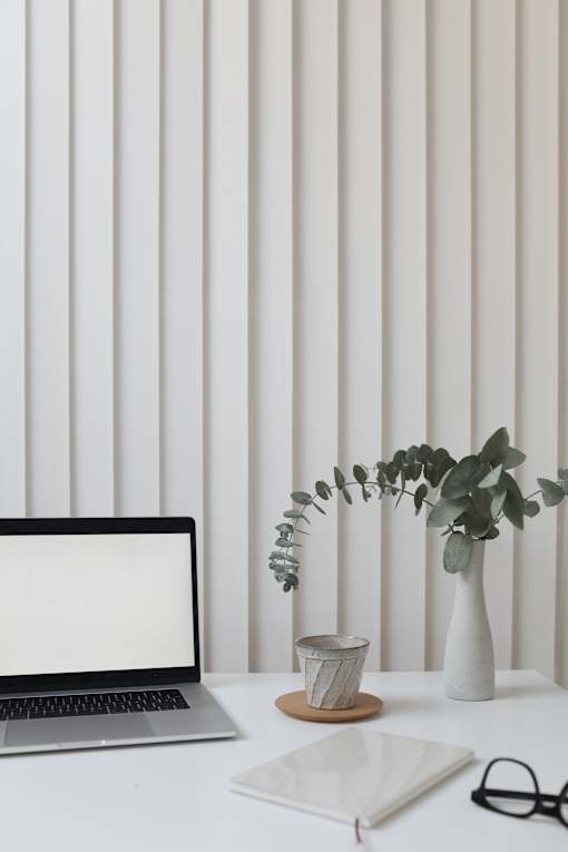 laptop on white desk with eucalyptus plant in white vase and gray coffee mug