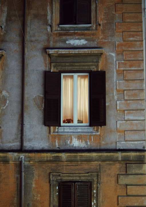A window with a white curtain and black shutters on a building.