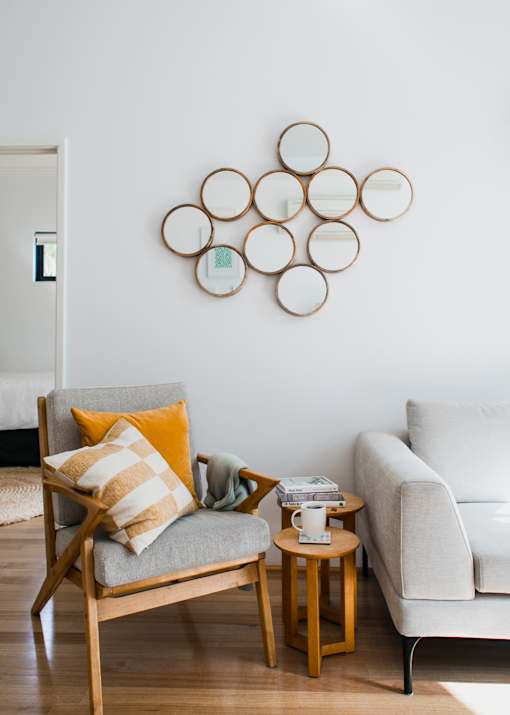 gray and wood chair with corner of couch, coffee table, and mirrors on white wall