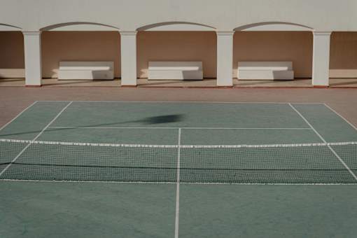 A tennis court with a net and white benches under a white building.
