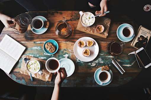 A table with various food items and drinks with a book and a person's hands.