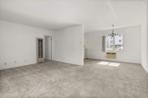 A large empty room with a carpeted floor and a chandelier hanging from the ceiling.