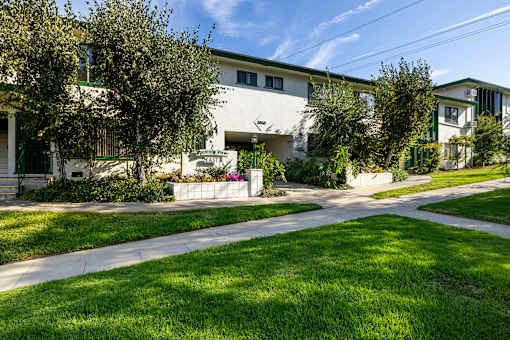 A white building with green trim and a sign that says "The Oaks" is surrounded by trees and grass.