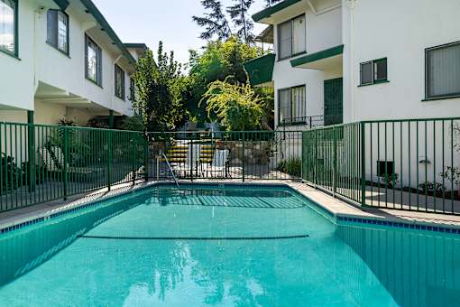 A swimming pool in front of a white building with green fencing.