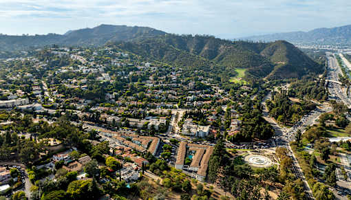 A cityscape with a mix of residential and commercial buildings, surrounded by hills and a highway.