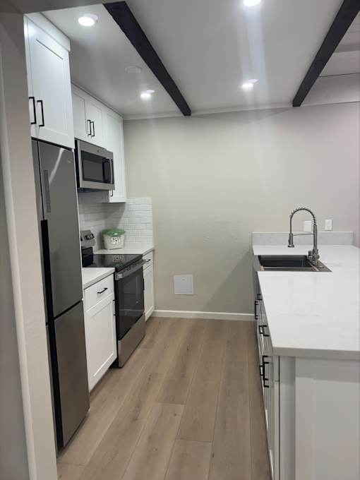 A kitchen with white cabinets and a black fridge.