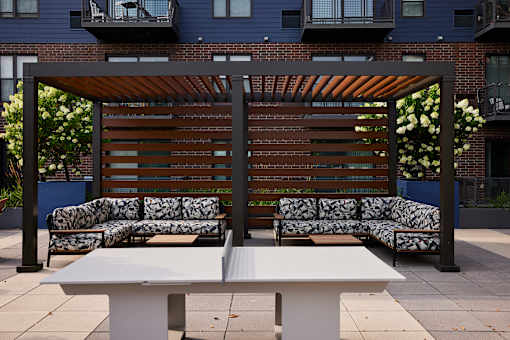 A white table is in front of a bench with a wooden backrest.