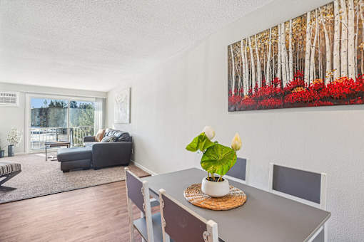A living room with a grey table and chairs, a grey sofa, a rug, and a painting on the wall.