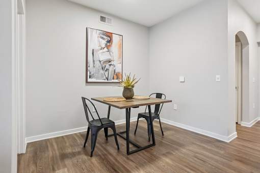 A dining room with a table and chairs and a painting on the wall.