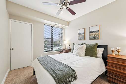 A bedroom with a bed, a ceiling fan, and a window with blinds.