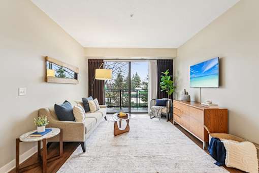 A living room with a couch, a coffee table, a TV, and a window with a view of trees.