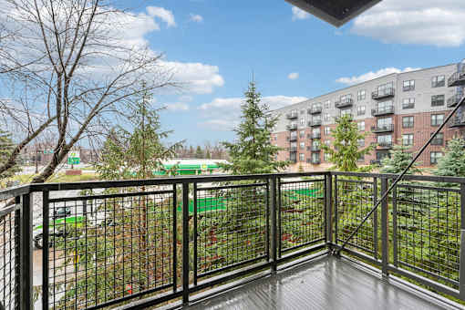 A balcony with a black railing overlooks a green lawn and a brick building.