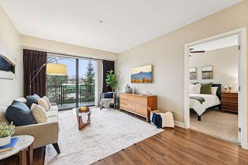 A living room with a couch, a chair, a coffee table, a painting, a bed, and a rug.