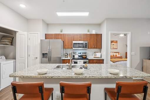 A kitchen with a granite countertop and brown chairs.
