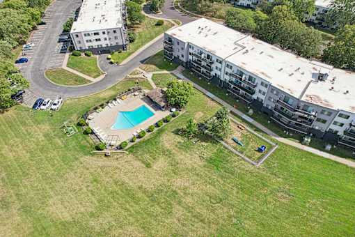 An aerial view of a large grassy area with a swimming pool and apartment buildings.