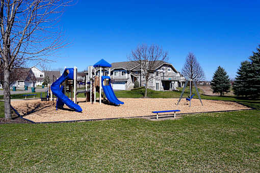 Community playground located on the property for time playing outside. Playground features two slides, a swing set, and multiple options of bench seating along the perimeter.