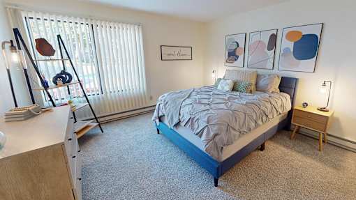 A bedroom with a bed, nightstand, and a window with blinds at The Bosk Apartment Homes, Woodbury, MN, 55125
