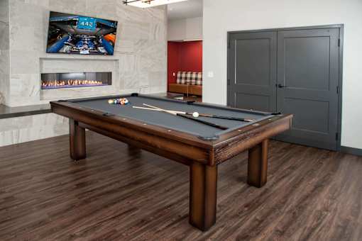 Pool table in community space across from fireplace and mounted TV.
