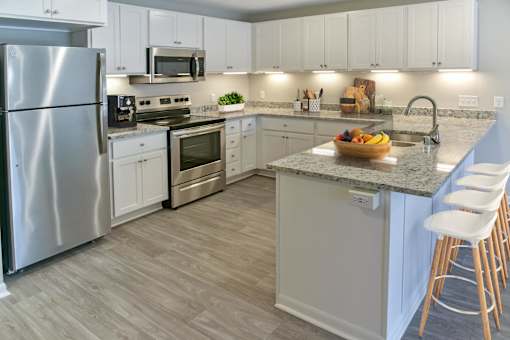 A kitchen with a refrigerator, microwave, oven, sink, and bar stools.