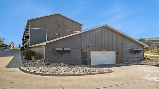 A large metal building with a garage door and a small tree in front.