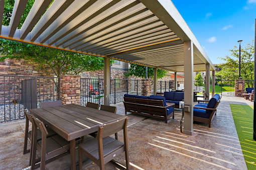 A wooden table and chairs are set up under a covered patio area.
