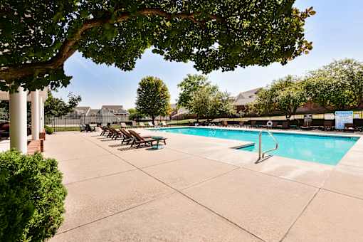 A pool surrounded by trees and chairs.