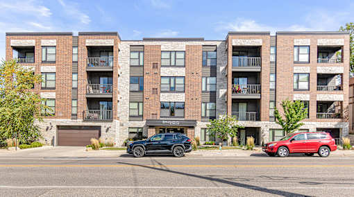 A black car is parked in front of a red car in front of a brick building.